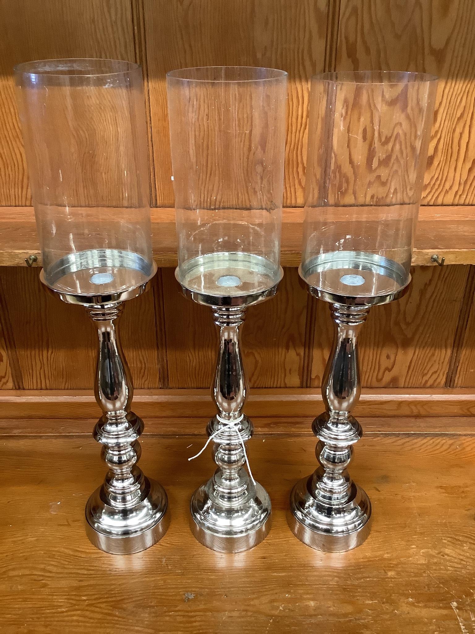 Set of three nickel plated candle stands with glass shades, height 51cm